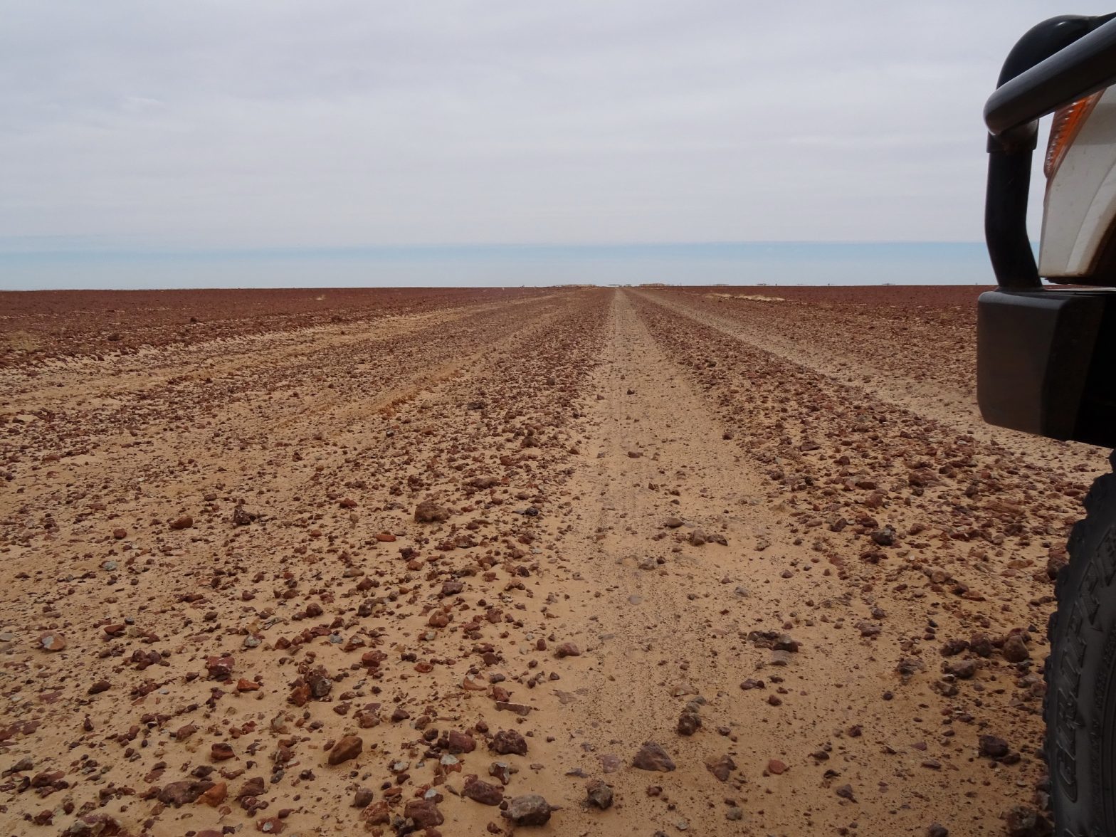 White four-wheel-drive staring down an empty dirt road in the Australian outback