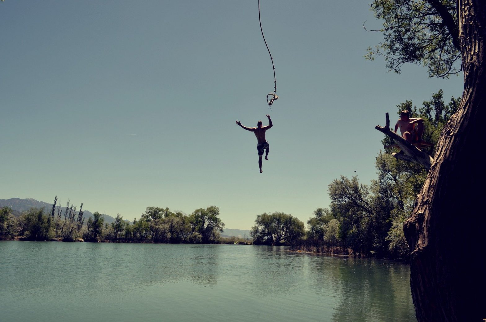 Man swinging from a rope into a creek
