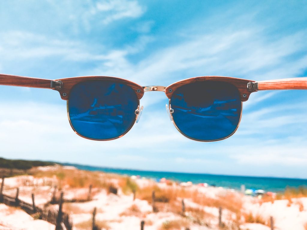 Pair of wooden frame ray-ban sunglasses looking toward a sandy beach. 