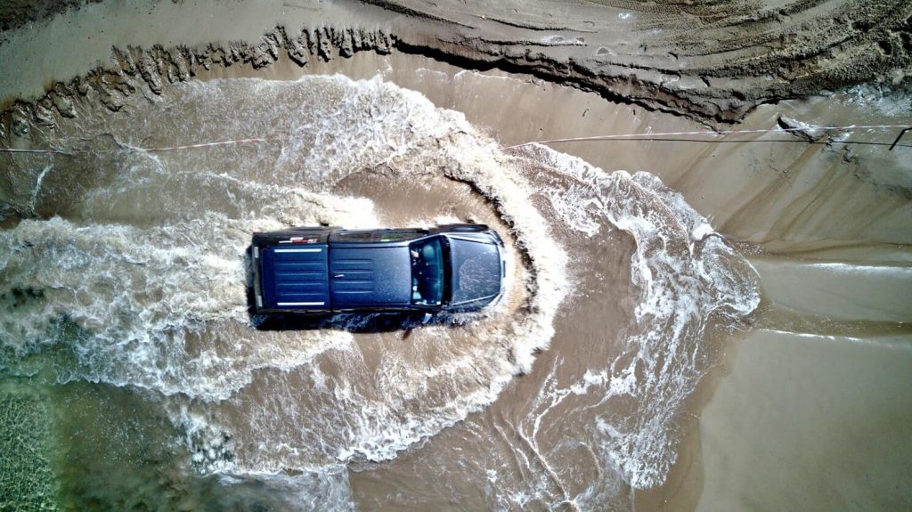 Arial view of a 4WD driving across a beach, in the water