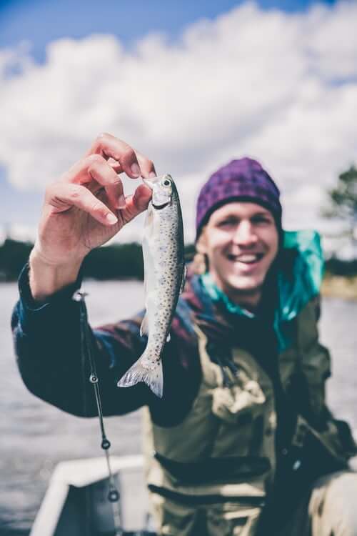 Man smiling and holding a freshly caught fish. 