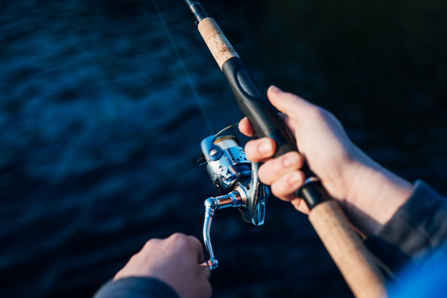 Close up of rod and reel as person fishes into deep blue waters.