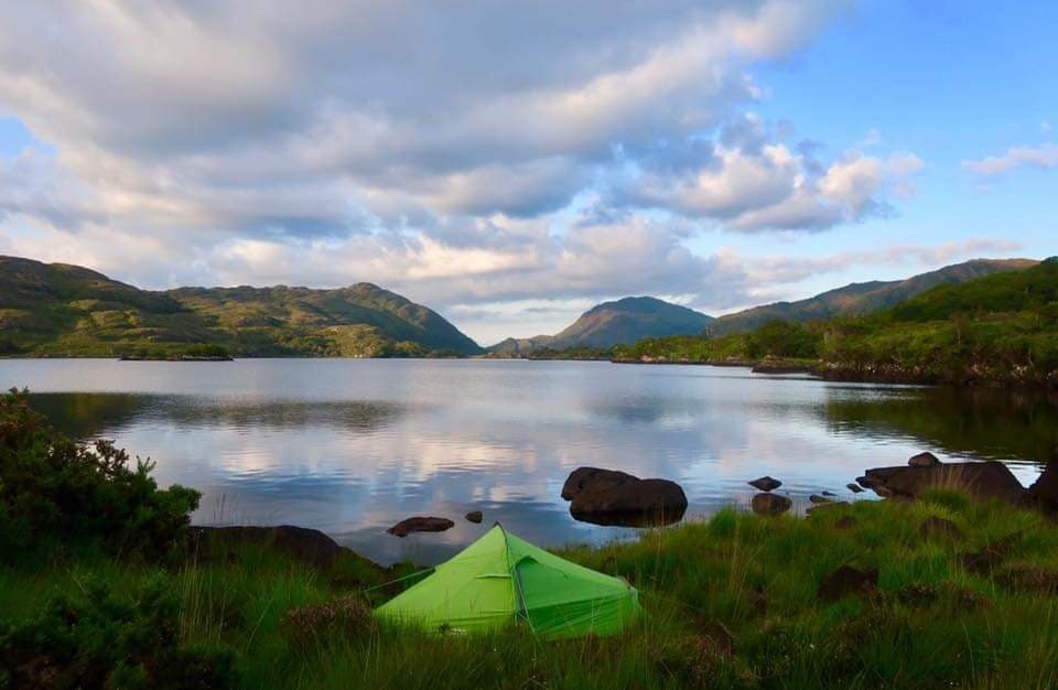 Green tent set up by a lake at dusk