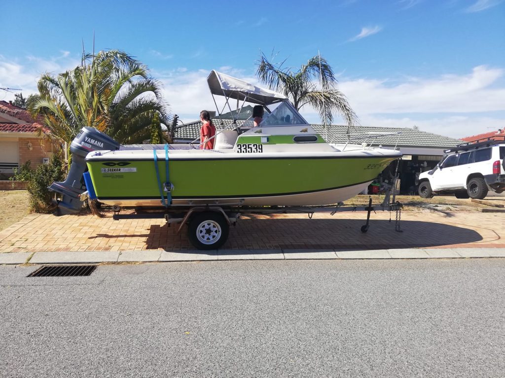 Green and white boat parked on trailer in driveway