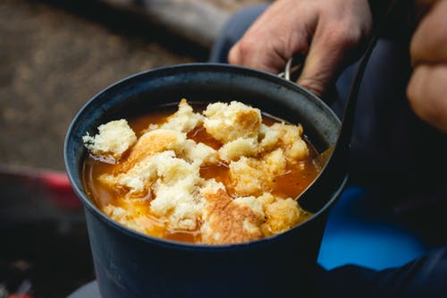 Hearty soup being heating in a pot over a campfire